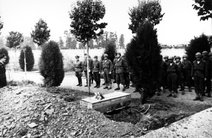 Members of the 94th Infantry Division, captured by the Germans at Lorient, France, stand in ranks during a funeral for one of their own held while they were POWs. Note the flowers on the crudely made wooden casket and the German officer standing at the far left side in the forefront.