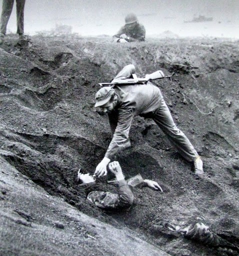 A carbine-carrying Marine places a cigarette between the lips of a half-buried Japanese soldier while a couple of buddies watch. Photo provided by Dick Honyak