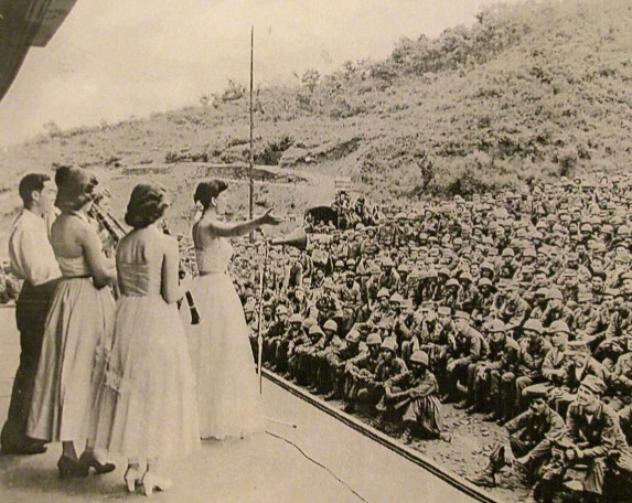 Cpl. Burton squats with his Speed Graphic camera in the bottom right-hand corner waiting to get a shot of a USO Troop visiting the 7th Division along the DMZ shortly after the end of the war in 1953. Photo provided by Roger Burton