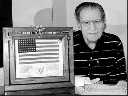 Former Sgt. Pete Chisholm who lives in Essex House, Port Charotte, Fla. is pictured with a 'Blood Chit' in a frame and his World War II ribbons and medals attached. The American flag with Chinese writing below was worn on the back of his flying jacket. Sun photo by Don Moore