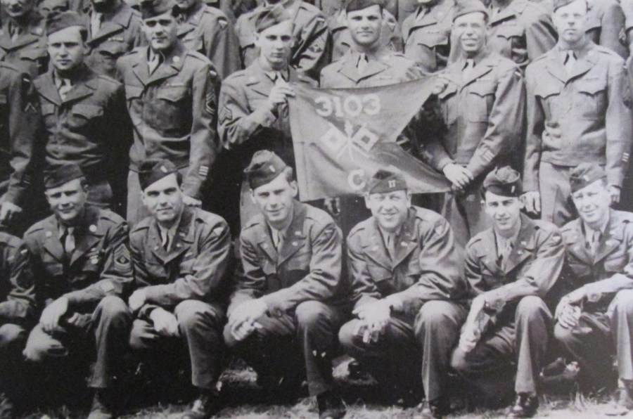 Spreading untruths: Members of the U.S. Army Signal Corps Company-C, 3103rd Battalion are pictured with their guidon. They helped Allied Forces turn the phony 1st U.S. Army Group into reality for the Germans during World War II. U.S. Cleveland of Punta Gorda is the young lieutenant squatting in the front row fourth from the right.