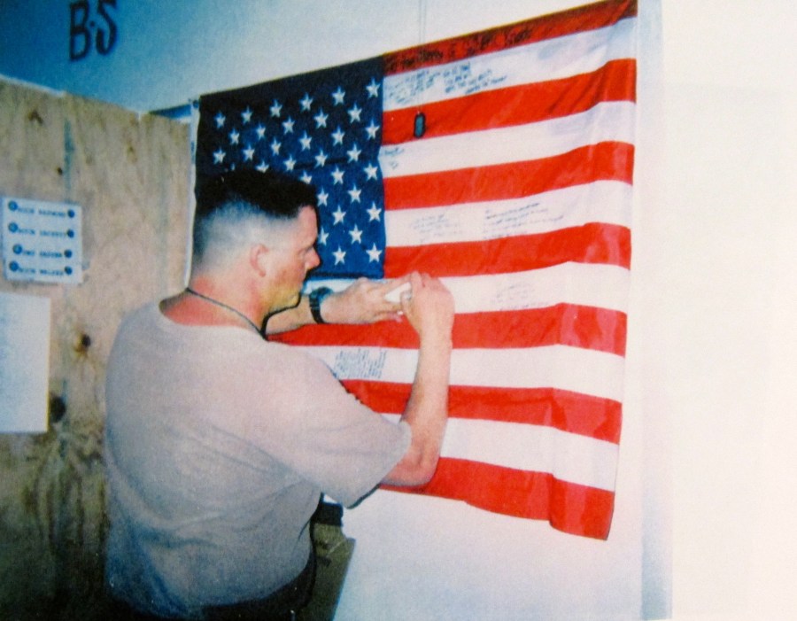 A Seabee signs an American flag for a fellow Seabee killed by an insurgent mortar round that was fired indiscriminately into Camp Falugah last September. The flag was being signed by many of the members of the dead Seabee’s construction battalion. It was sent home to his parents. Photo by David Frey