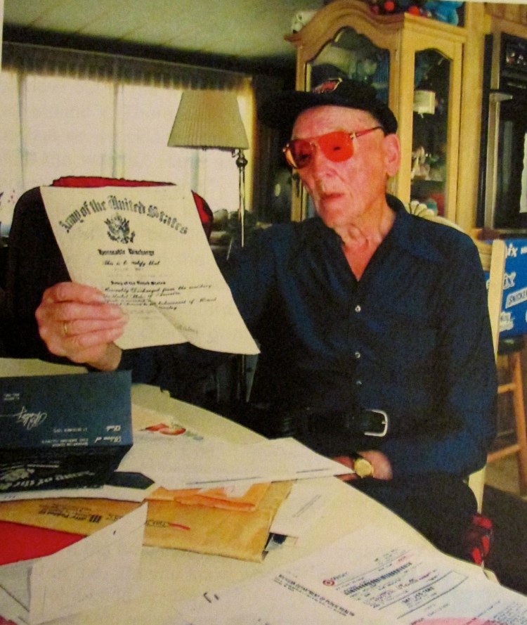Roland Hardt, of El Jobean, looks at his Honorable Discharge that notes he received a Purple Heart, the Belgium Medal of Honor and five bronze Battle Stars for five major battles: Normandy, the Ardennes, North France, Rhineland and the Philippine Liberation Ribbon. Sun photo by Don Moore