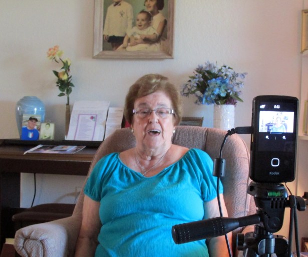 Katherine Riposta tells husband’s war story during a DVD filming in her Deep Creek apartment. Frank is in the blue urn in the background on the piano to the left of her. Sun photo by Don Moore